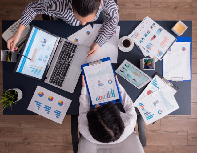 Top viewTop view of manager and employee doing teamwork in business office , looking at charts on laptop display. Finance paperwork with charts at workplace. Discusing financial plan.