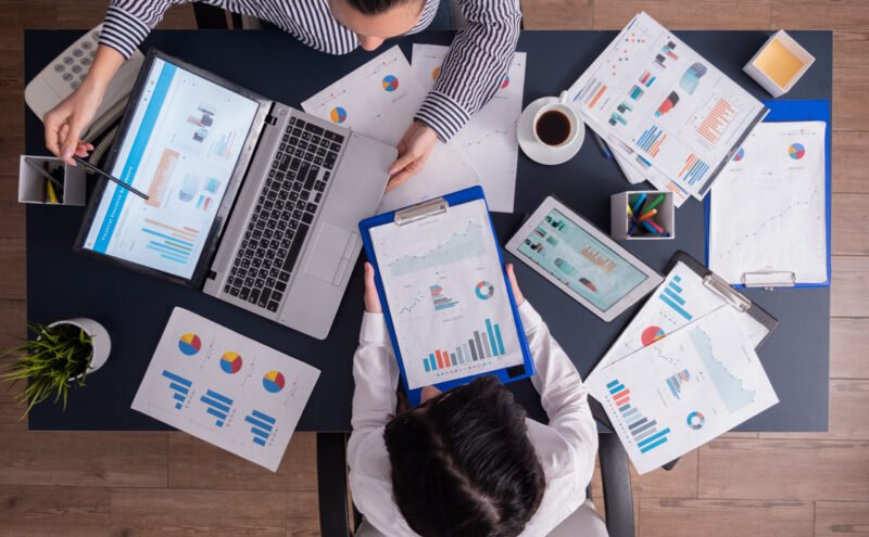 Top viewTop view of manager and employee doing teamwork in business office , looking at charts on laptop display. Finance paperwork with charts at workplace. Discusing financial plan.